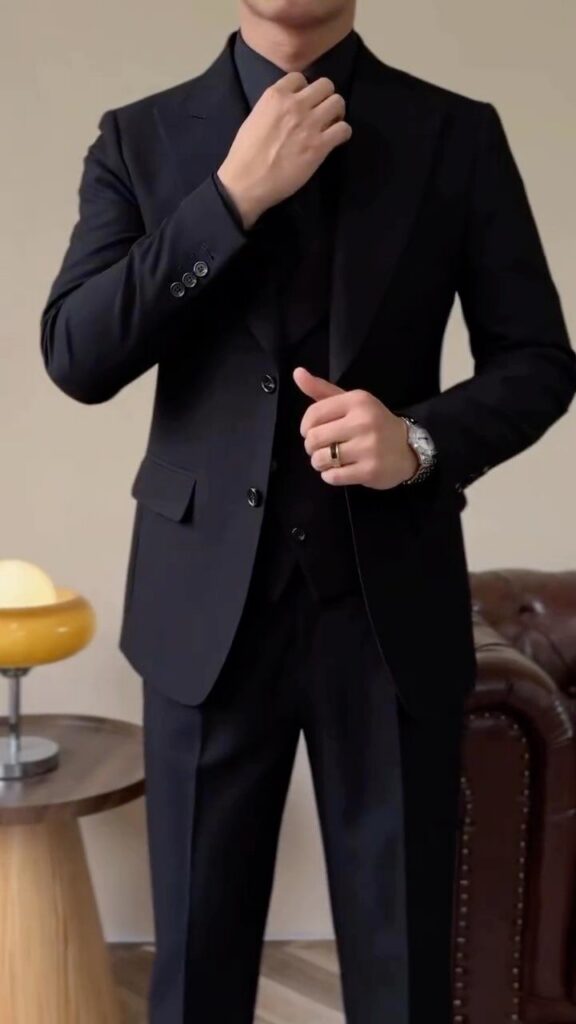 Man in a formal black suit adjusting his collar while wearing a silver watch.