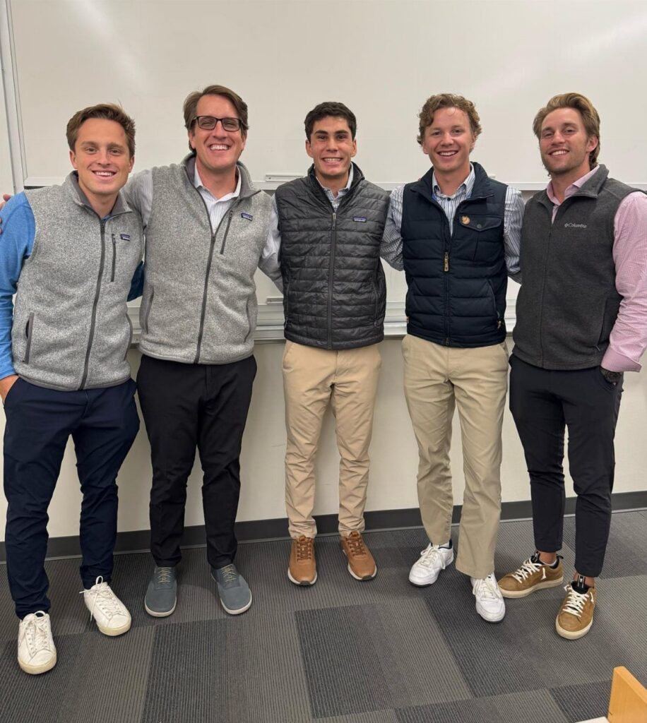 Five men standing in a row wearing various styles of vests and casual clothing.