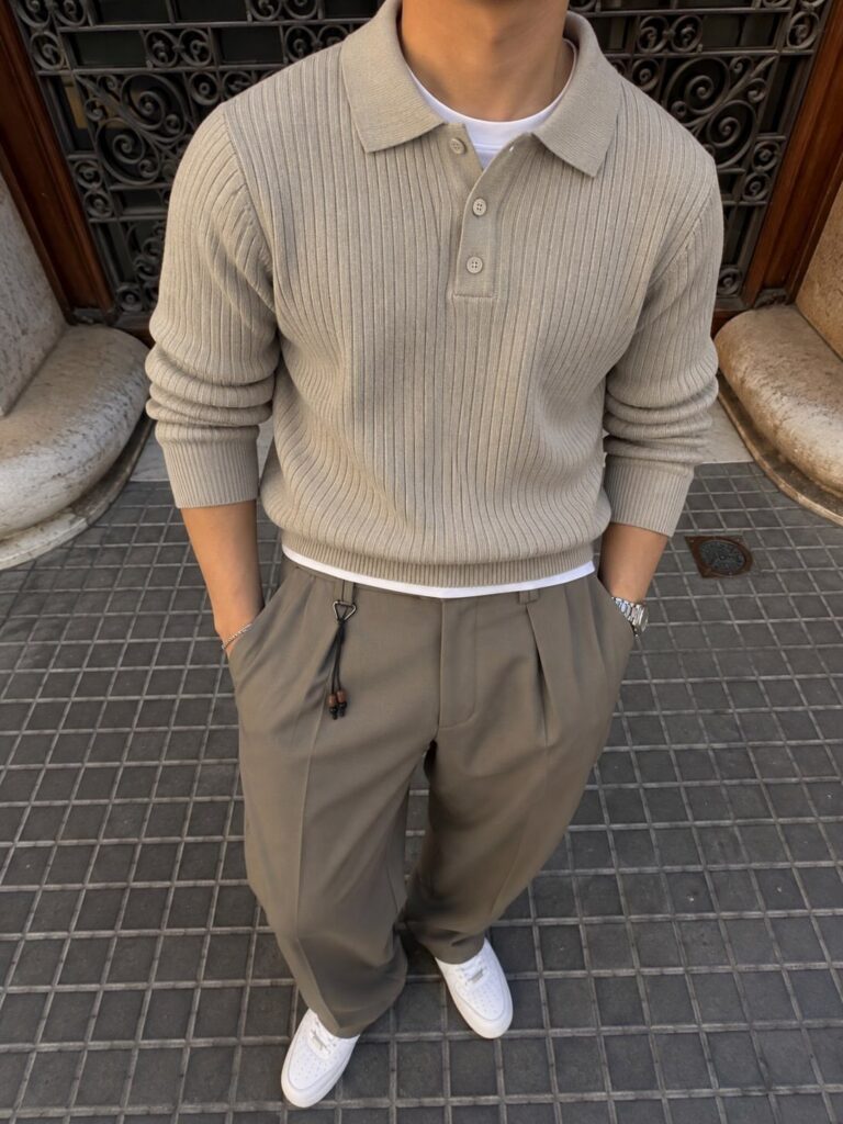 A person wearing a beige ribbed polo sweater and olive green trousers with white sneakers.