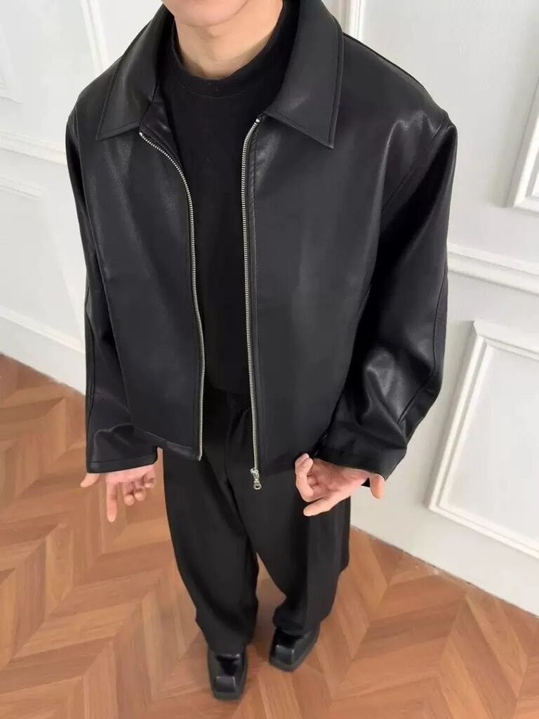 A person wearing an oversized black leather jacket, black t-shirt, and black trousers.