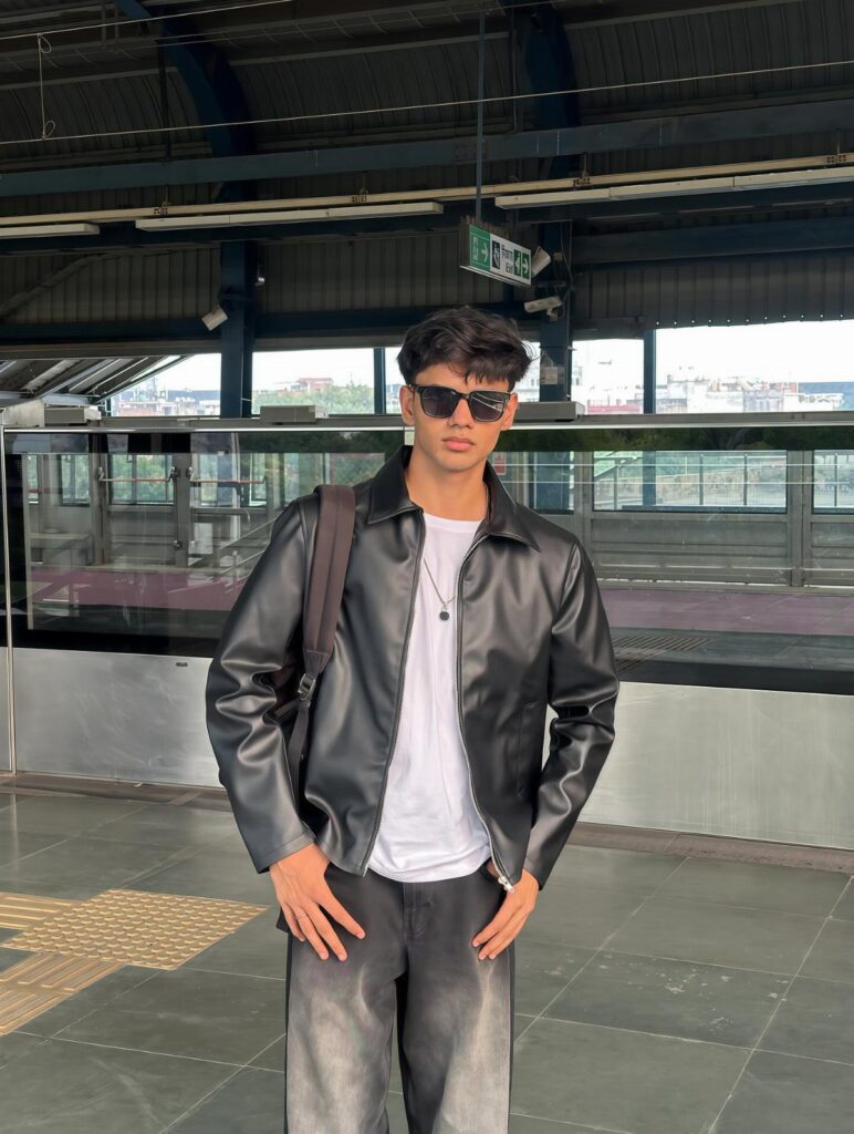 Young man in a black leather jacket and white t-shirt standing on a platform.