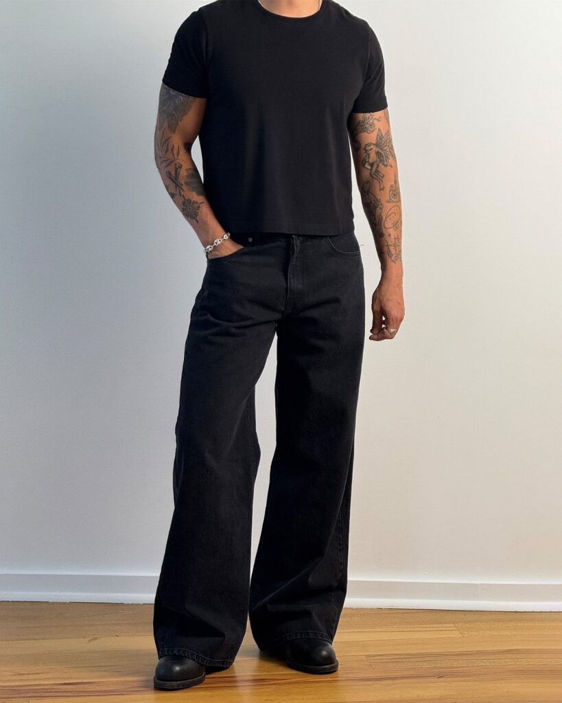 A person wearing a black fitted t-shirt and wide-leg black denim jeans.