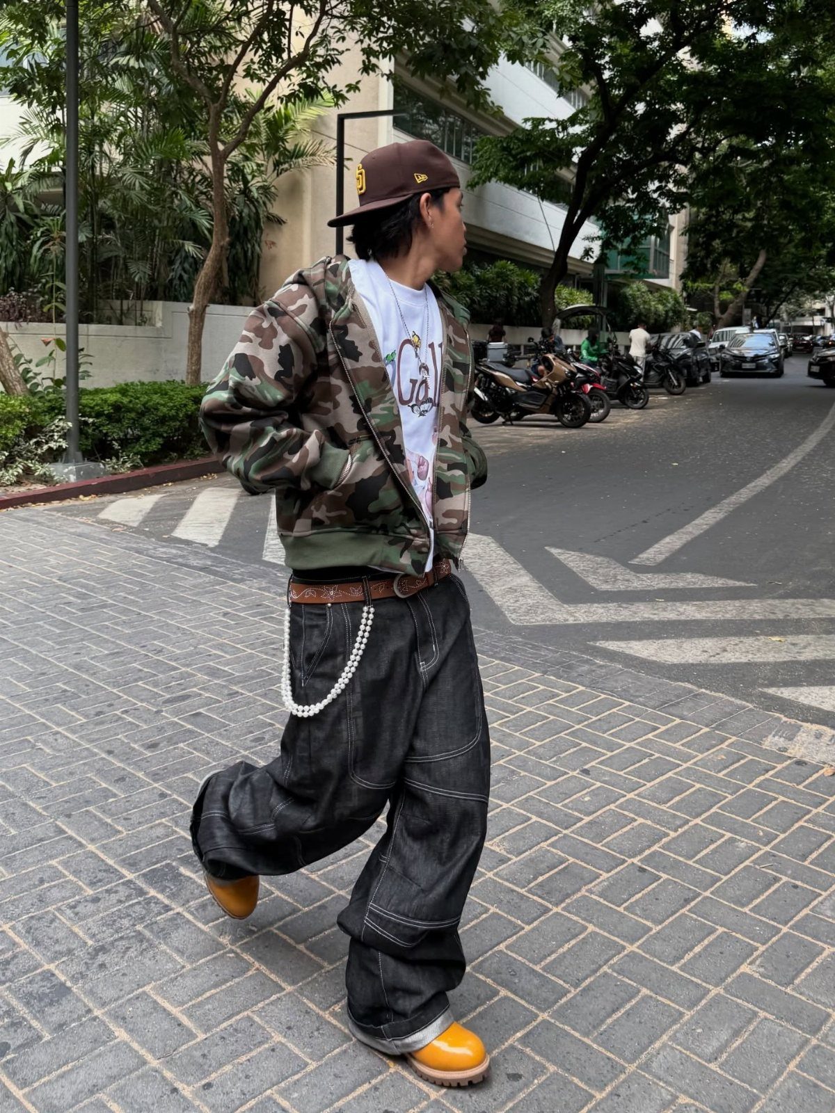 A person walking down a street wearing a camouflage jacket and baggy dark denim jeans.