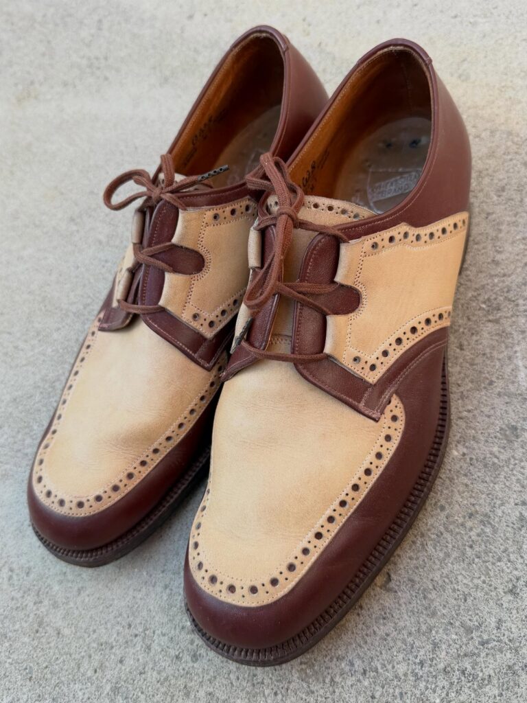 Two-tone tan suede and dark brown leather wingtip derby shoes on a grey surface.
