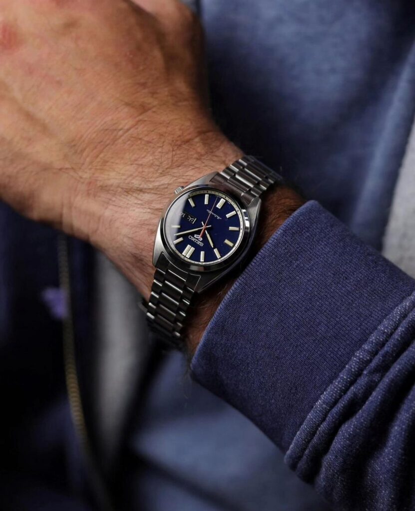 A silver metal watch with a dark blue face worn on a man's wrist.