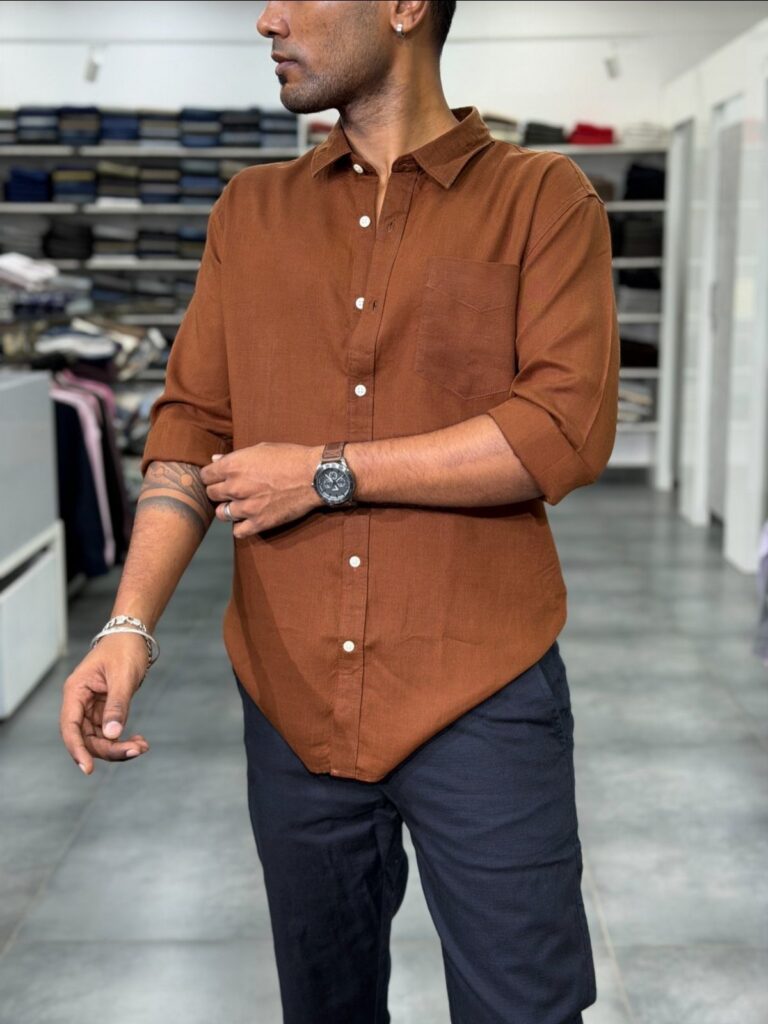Man wearing a burnt orange button-down shirt paired with dark navy blue trousers.