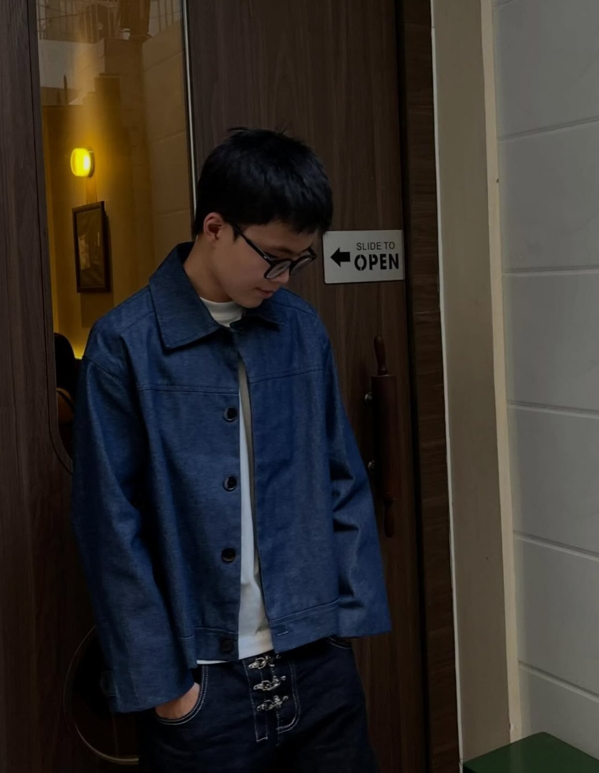 Young person wearing a blue denim jacket over a white t-shirt and dark jeans.