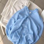 A light blue linen button-up shirt and cream trousers laid on a white chair.