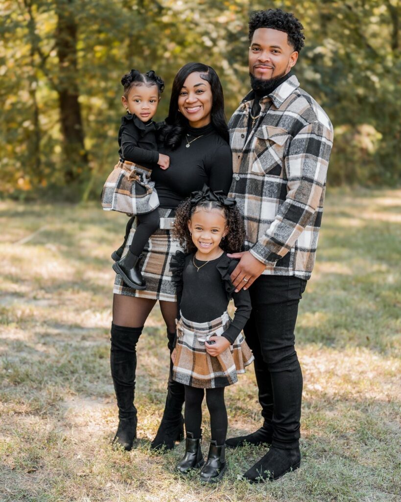 A family of four posing together in coordinated black and plaid autumn outfits outdoors.