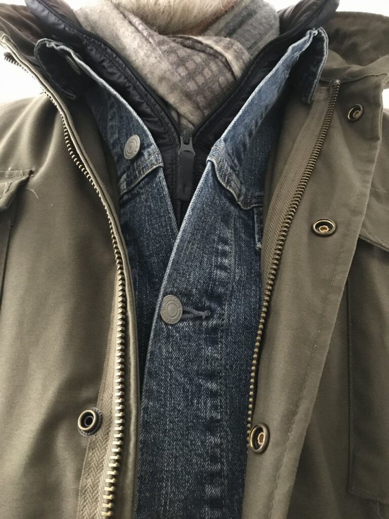 Layered clothing including an olive parka, denim jacket, and a grey scarf.