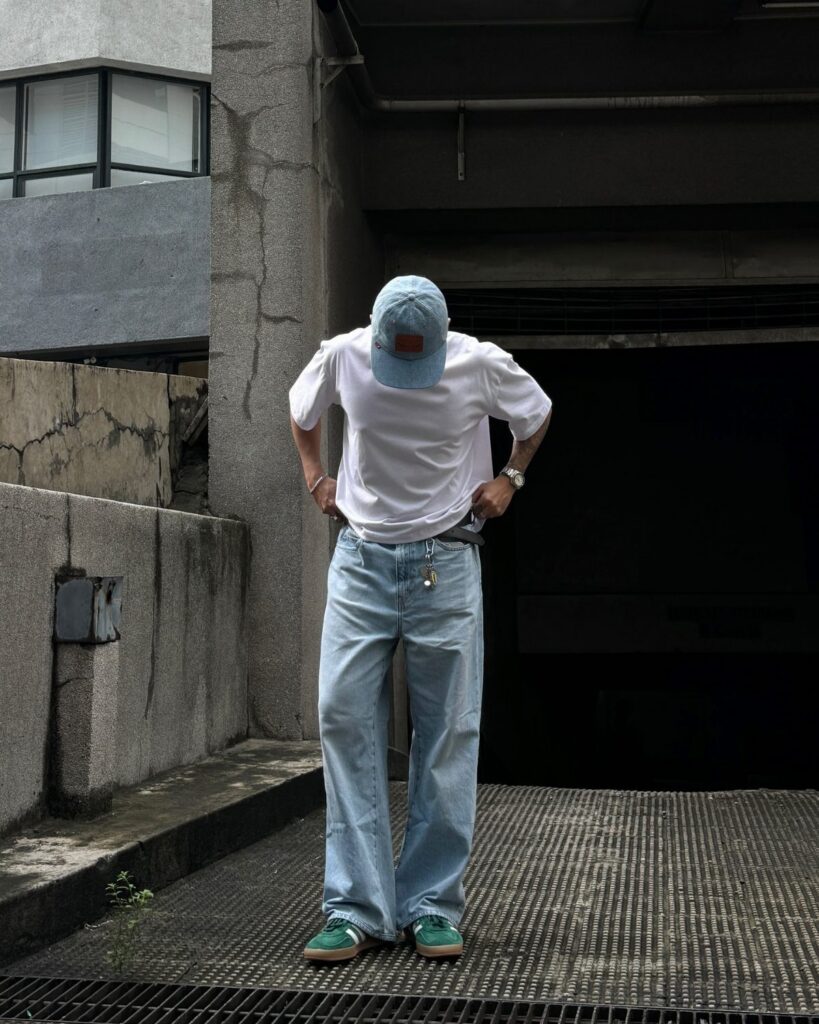 Person wearing a white t-shirt, light blue jeans, and green sneakers standing outdoors.