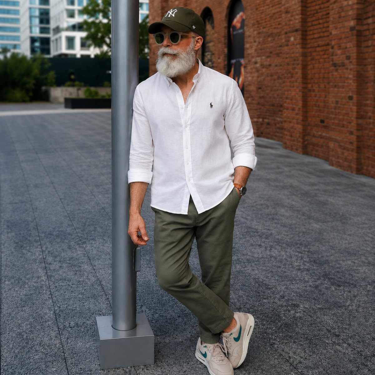 A stylish older man with a white beard wearing a white shirt and olive trousers.