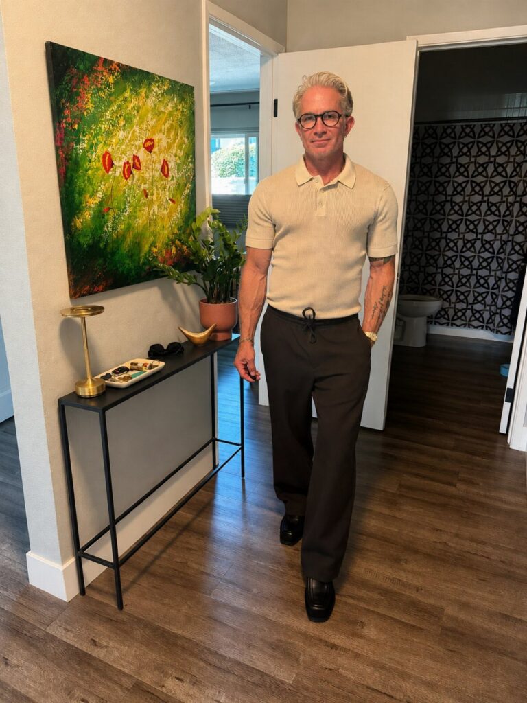 A middle-aged man posing in a beige polo shirt and black trousers in a hallway.