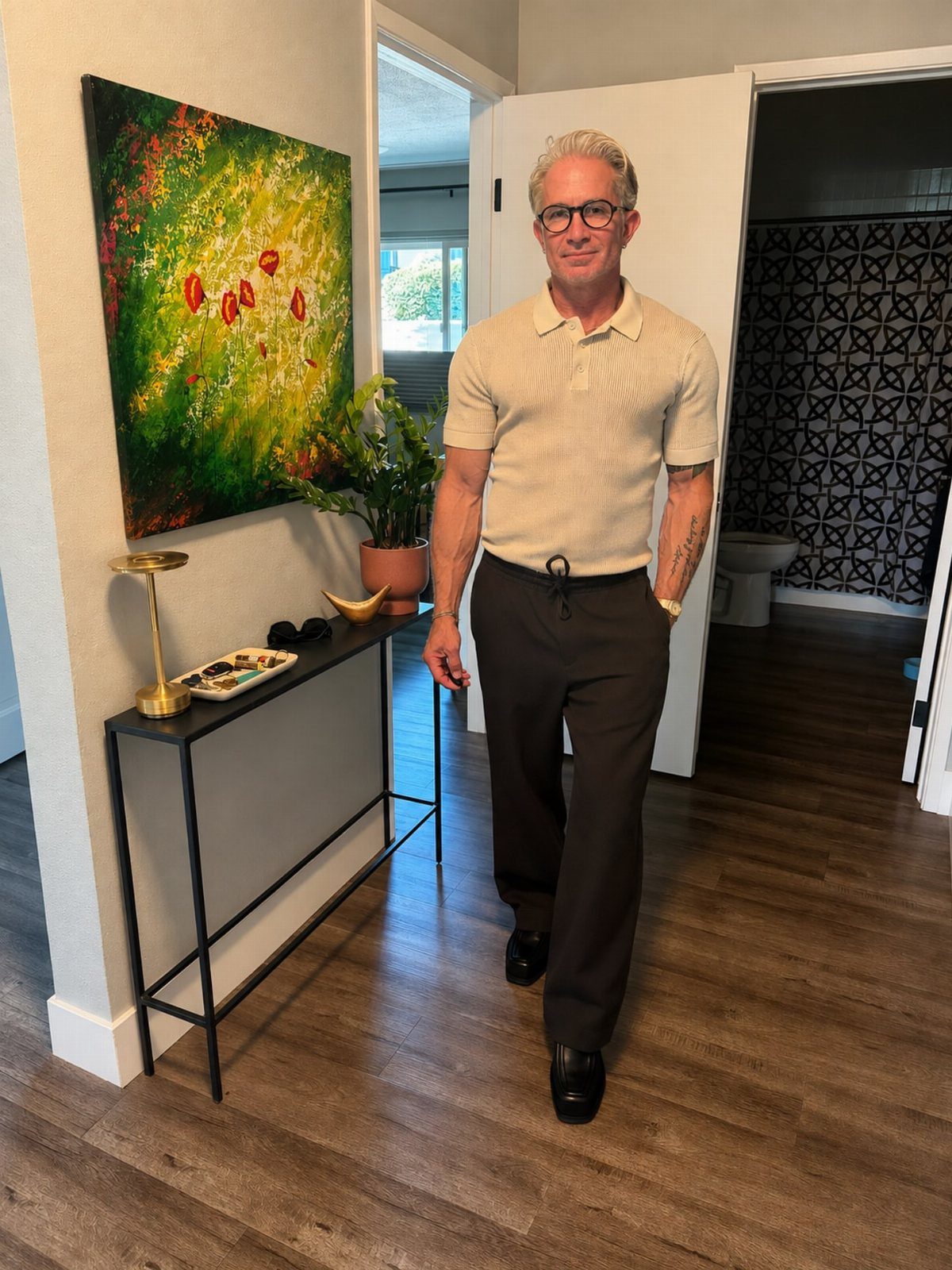 A middle-aged man posing in a beige polo shirt and black trousers in a hallway.