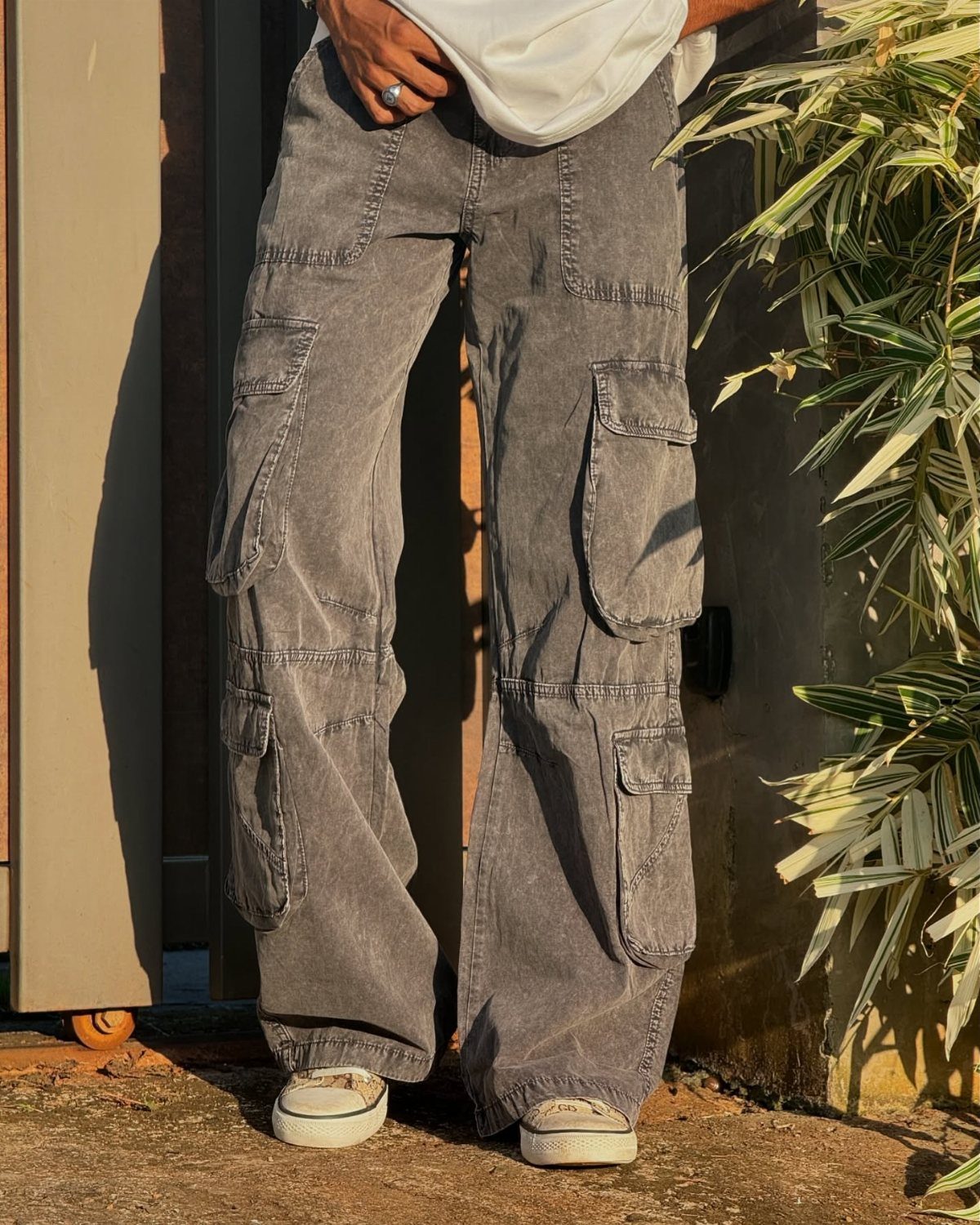 A person wearing wide-leg grey cargo pants with large utility pockets and white sneakers.