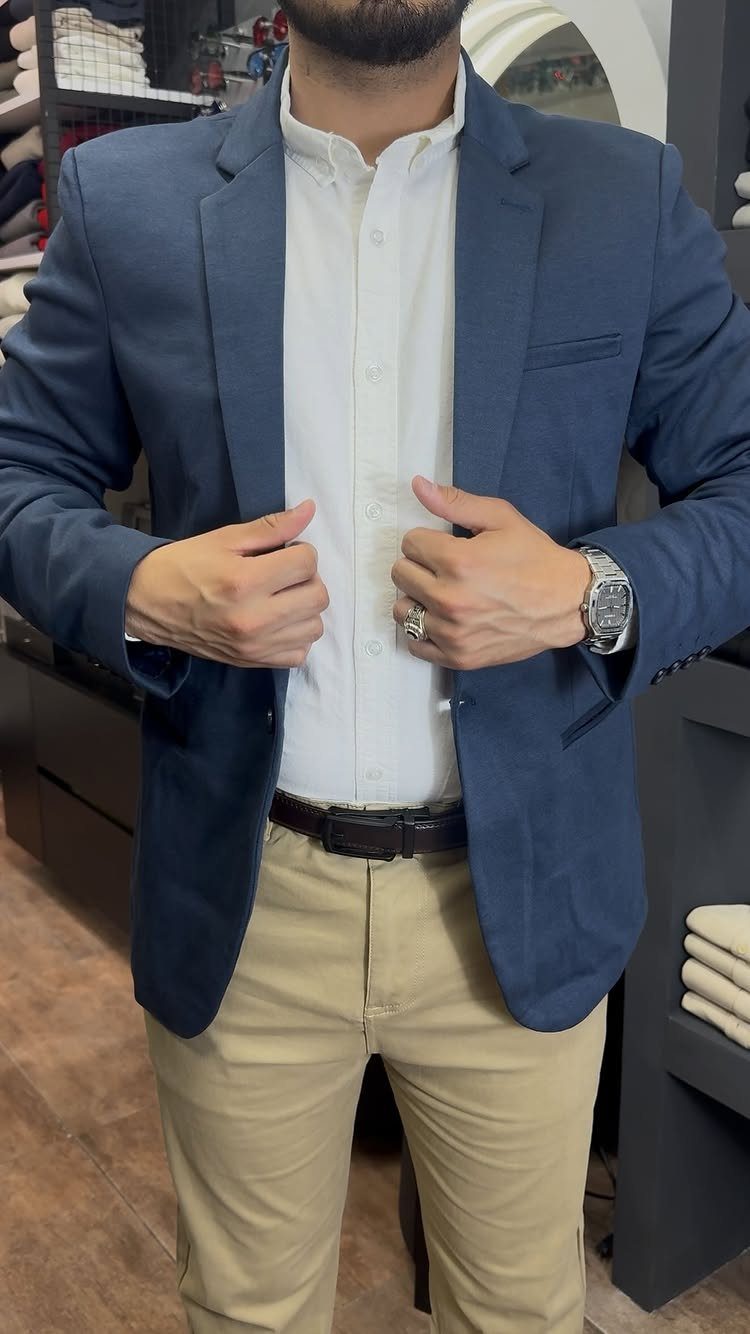 Man wearing a blue blazer, white shirt, and tan chinos in a clothing store.