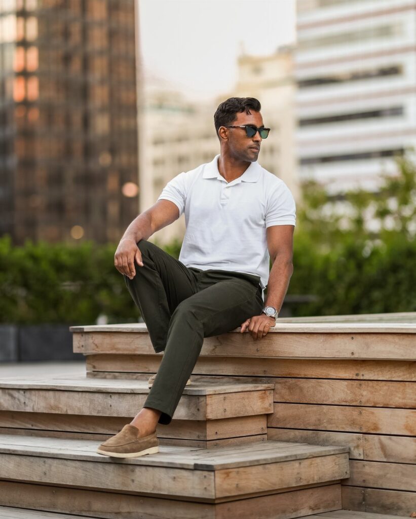 Man in a white polo shirt and olive green chinos sitting on wooden steps.