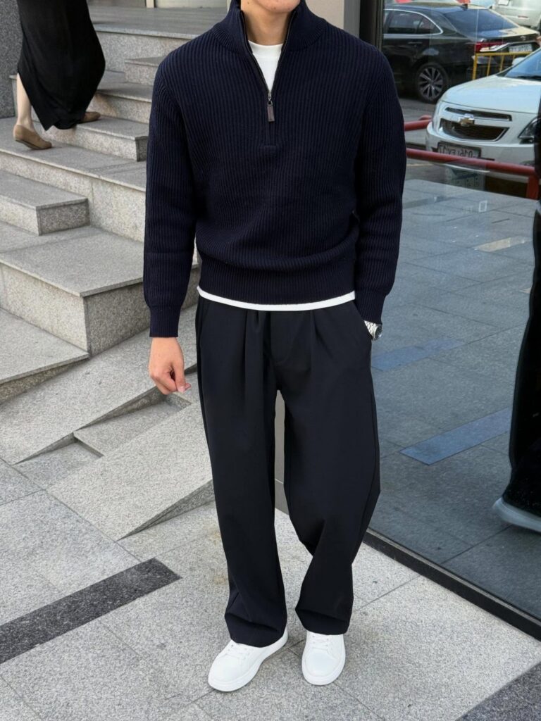 Man wearing a navy ribbed quarter-zip sweater, navy trousers, and white sneakers standing on stairs.