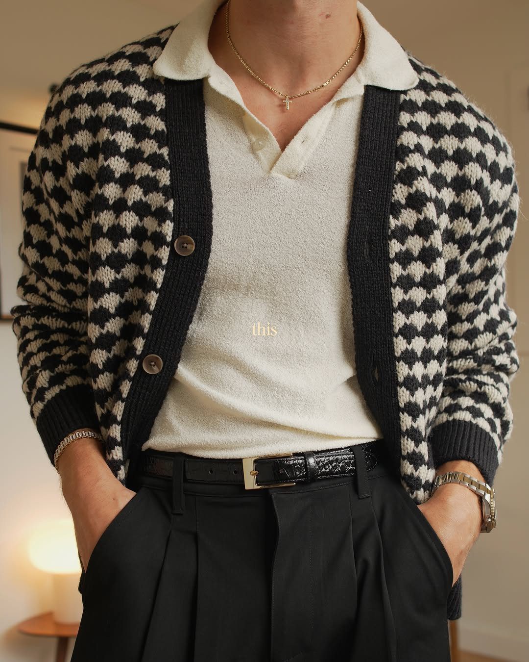 Man wearing a houndstooth cardigan over a cream polo sweater and black trousers.